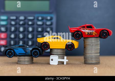 Miniaturautos auf Münzen gestapelt mit Schlüssel und Rechner im Hintergrund. Stockfoto