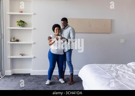 Ein Paar zu Hause lächelt, während es im Schlafzimmer gemeinsam auf das Smartphone schaut Stockfoto