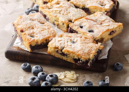 Blueberry Breakfast Cake strotzt vor frischen Beeren und wird von knusprigen Mandelsplittern aus der Nähe auf dem Holzbrett auf dem Tisch gekrönt. Horizontal Stockfoto