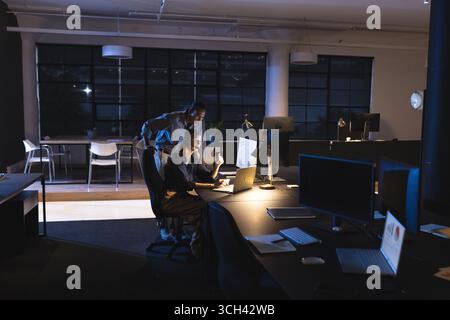 Kollegen, die spät im Büro arbeiten und gemeinsam Daten auf dem Computerbildschirm analysieren Stockfoto