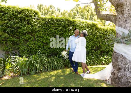Seniorenpaar, das sich unter einem Baum im Garten umschließt und einen romantischen Moment miteinander genießt Stockfoto