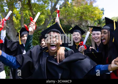 Absolventen mit Diplomen, Mützen und Kleidern, feiern im Freien Stockfoto