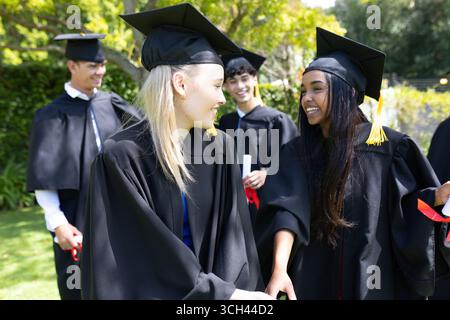 Die Studenten feiern in Mützen und Kleidern und lächeln fröhlich im Freien Stockfoto