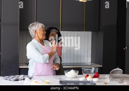 Backen in der Küche, Afroamerikanerin und ältere Frau teilen gemeinsam Lachen Stockfoto