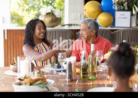 Wir feiern den Ruhestand, die afroamerikanische Familie lacht und redet am Esstisch Stockfoto