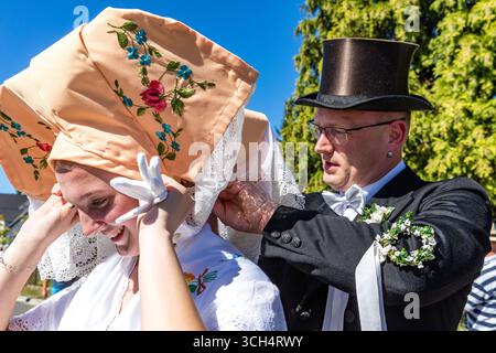 31. August 2025, Brandenburg, Burg (Spreewald): Eine Teilnehmerin in traditioneller Burger-Hochzeitskostüm bei der Trachtenparade im Rahmen des Lokal- und Trachtenfestes hilft einer Teilnehmerin bei der Anpassung ihrer Kapuze. Foto: Frank Hammerschmidt/dpa Stockfoto