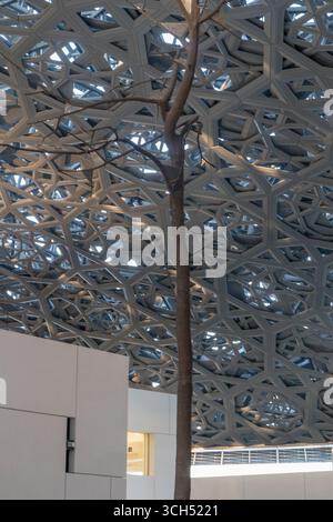 VAE - Abu Dhabi - Louvre Abu Dhabi - schlanker Innenhofbaum, der sich unter dem kühlen Schatten des geometrischen Baldachins erhebt Stockfoto