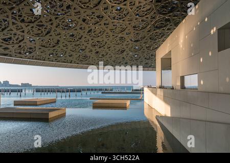 VAE - Abu Dhabi - Louvre Abu Dhabi - Innenhof am Ufer mit schwimmenden Plattformen unter einem weitläufigen, gemusterten Baldachin in der Abenddämmerung Stockfoto