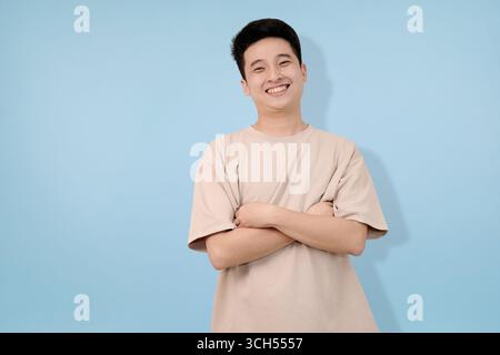 Junger Mann mit Freude und überkreuzten Armen posieren im Studio-Hintergrund Stockfoto