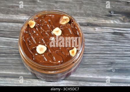Schokoladencreme mit Kuchen, gekrönt mit Schokoladenpaste und Haselnussstücken und mit Kuchen überzogen, ein weiches, zubereitetes Essen mit Schichten geschlagener Crea Stockfoto