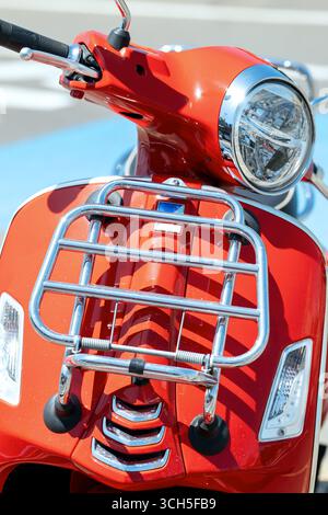 Vorderansicht eines klassischen roten Rollers mit Chrom-Details, geparkt in der Nähe einer Fußgängerbrücke; stilvoller Stadtverkehr mit Vintage-Flair. Stockfoto