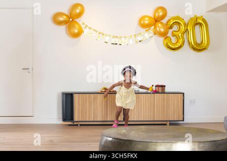 Afroamerikanisches Kind, das mit Goldballons und Banner im Wohnzimmer Bananen hält Stockfoto