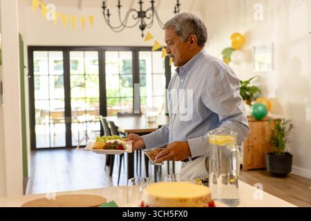 Mann im mittleren Erwachsenenalter, der sich selbst an einem Partybuffet im Haus serviert, mit Trauben und Käse, Kopierraum Stockfoto