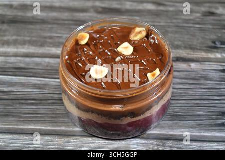 Schokoladencreme mit Kuchen, gekrönt mit Schokoladenpaste und Haselnussstücken und mit Kuchen überzogen, ein weiches, zubereitetes Essen mit Schichten geschlagener Crea Stockfoto