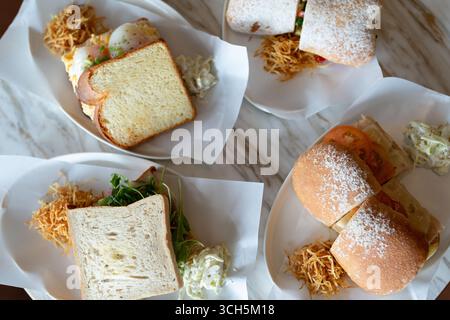 Tisch in einem gemütlichen Café, mit einer Auswahl an Sandwiches auf Tellern, einschließlich auf halbierten Brötchen und gerösteten Brotscheiben, hervorgehoben d Stockfoto