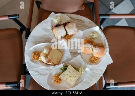 Tisch in einem gemütlichen Café, mit einer Auswahl an Sandwiches auf Tellern, einschließlich auf halbierten Brötchen und gerösteten Brotscheiben, hervorgehoben d Stockfoto