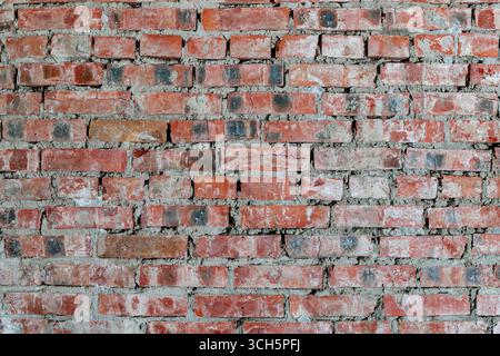Nahaufnahme einer alten roten Ziegelmauer mit rauem Mörtel und verwitterter Oberfläche. Rustikaler industrieller Hintergrund. Stockfoto