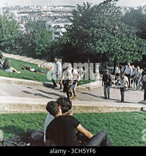 Rückansicht eines Paares und Touristen, die die Stufen des Montmartre hinaufsteigen, während sich Paris in der Ferne erstreckt, aufgenommen auf Analogfilm. Stockfoto