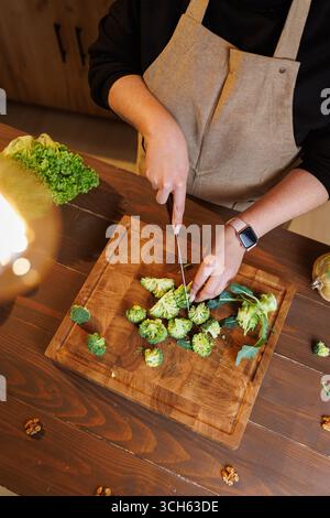Frischer Brokkoli wird auf einem hölzernen Schneidebrett in gemütlicher Küche geschnitten Stockfoto