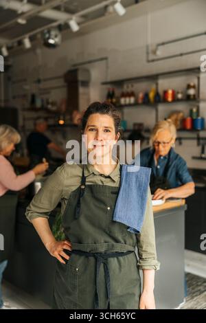 Porträt einer selbstbewussten Küchenchefin, die während des Kochkurses in der gewerblichen Küche mit Hand auf Hüfte steht Stockfoto