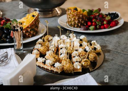 Eleganter Catering-Teller mit Waffelkanapees, Käsebällchen und exotischem Obst auf dem Tisch Stockfoto