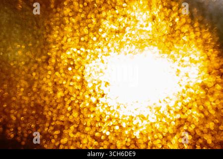 Verschwommene und abstrakte goldene Textur kondensierter Wassertröpfchen auf der Fensteroberfläche, die von hinten durch Sonnenlicht beleuchtet wird. Stockfoto
