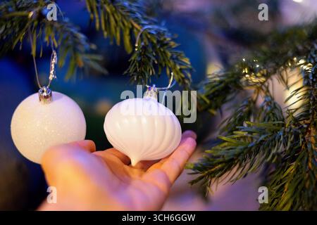 Schöne und elegante Weiße Weihnachtsschmuck Hang on Tree Frau Hand hält Ball Silvester Grün Kiefer Feiertagsatmosphäre Vorbereitung Stockfoto