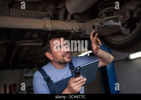 Mechaniker, der das Fahrgestell mit einem digitalen Tablet in der Autowerkstatt überprüft Stockfoto