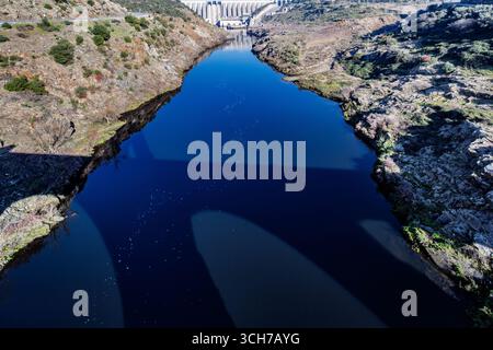 Eine römische Brücke wirft einen Schatten über den Fluss Tejo, mit dem Alcántara-Staudamm im Hintergrund, der technische Wunder hervorhebt. Stockfoto