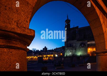 Die Kirche San Martin steht majestätisch bei Sonnenuntergang, wunderschön eingerahmt vom Bogen der Plaza Mayor in Trujillo, Extremadura, Spanien. Stockfoto