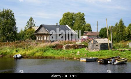 Rustikales Holzhaus am Fluss altes russisches Dorf mit Booten unter blauem Himmel in Karelien, Reisekonzept in Nordrussland Stockfoto