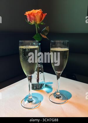 Zwei elegante Gläser Champagner und eine einzelne Rose in einer Vase auf einer weißen Tischdecke symbolisieren eine romantische Feier. Stockfoto