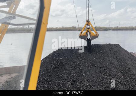 Kohleverladung per Kran auf einen Lastkahn auf dem Fluss, nördliche Lieferung entlang der Jenisei in Russland. Ein Baggerkran mit Kohleeimer schwebt Stockfoto
