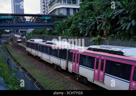 Ein moderner roter Personenzug fährt entlang der Bahngleise in einer belebten Stadt Stockfoto