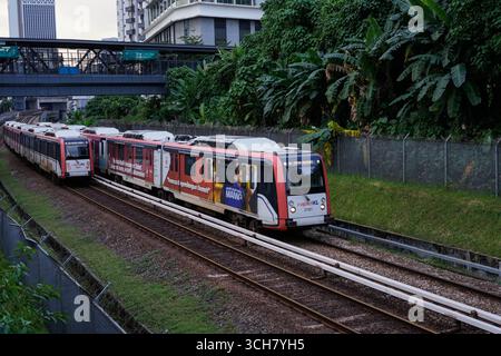 Ein moderner roter Personenzug fährt entlang der Bahngleise in einer belebten Stadt Stockfoto