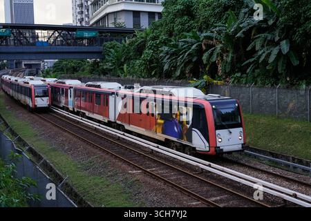 Ein moderner roter Personenzug fährt entlang der Bahngleise in einer belebten Stadt Stockfoto