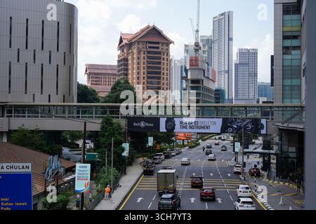 Am 16. september 2025 fotografieren Sie eine lebhafte Stadtszene mit Straßen, hohen Wolkenkratzern und einer Fußgängerbrücke mit großem Banner in Kuala Lumpur Stockfoto