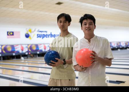 Zwei Freunde stehen in einer hellen Bowlingbahn, jeder hält einen bunten Ball. Stockfoto