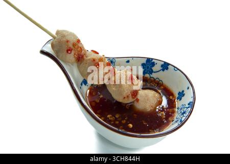 Gegrillte Fleischbällchen auf einem Spieß serviert mit thailändischer würziger Chili-Dipping-Sauce in einer floralen Keramikschale auf weißem Hintergrund. Stockfoto