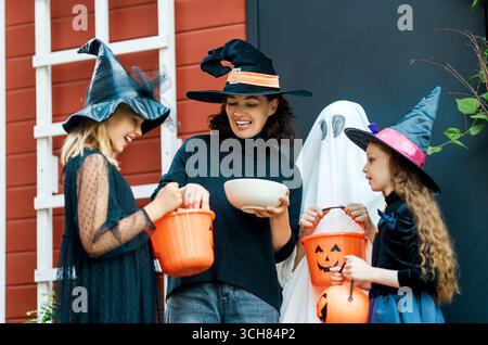 Glückliche Leute feiern Halloween. Erwachsene behandelt Kinder im Freien mit Süßigkeiten. Stockfoto