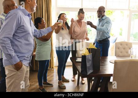 Gruppe verschiedener Seniorenfreunde, die zu Hause mit Getränken und Geschenken feiern und freudige Momente teilen. Feier, Ruhestand, Versammlung, Freundschaften, PR Stockfoto