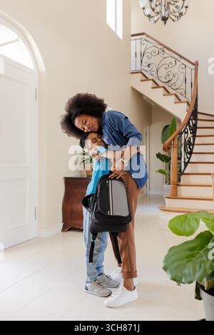 Mutter und Sohn umarmen sich zuhause warm und halten Schulrucksack in der Nähe der Treppe Stockfoto