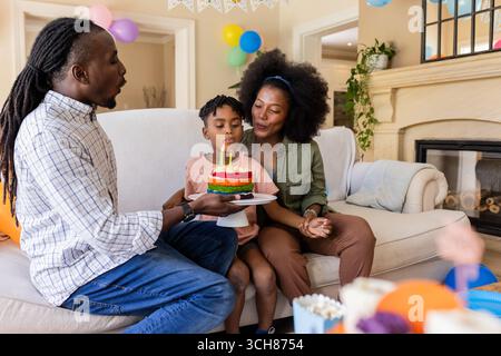 Afroamerikanische Familie feiert zu Hause Geburtstag, Kind bläst Kerzen aus Stockfoto