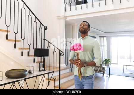 Ein Mann mit rosa Blumen, der in einem modernen Zuhause steht, nachdenklich aussieht, Kopierraum Stockfoto