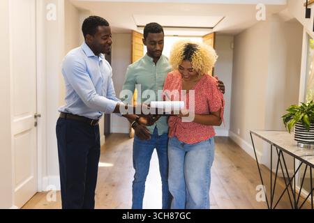Ein Paar und ein afroamerikanischer Immobilienberater diskutieren über ein neues Zuhause im Flur Stockfoto