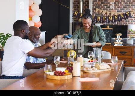 Wir feiern den Ruhestand, die afroamerikanische Familie teilt zu Hause Essen und lacht Stockfoto