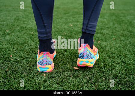 Nahaufnahme farbenfroher Laufschuhe auf grünem Gras. Person in Sportbekleidung, die nach dem Training im Freien steht Stockfoto
