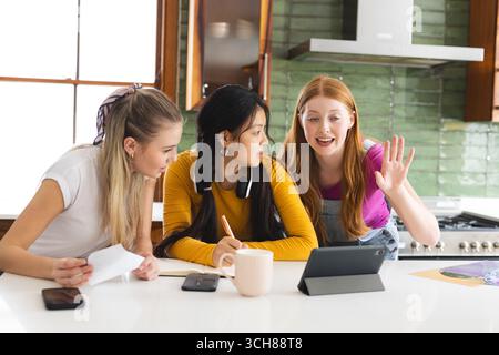 Teenagerinnen lernen zusammen in der Küche, benutzen Tablets und machen Notizen Stockfoto