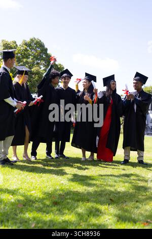 Abschlussschüler in Mützen und Kleidern, die an sonnigen Tagen mit Diplomen feiern Stockfoto