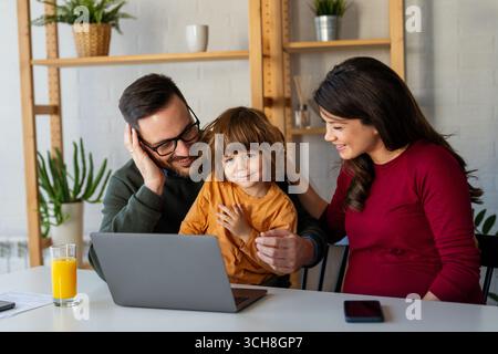 Glückliche Familie mit Kind, die Spaß beim gemeinsamen Gebrauch des Laptops hat, Eltern und Kind lachen sich zu Hause entspannt Stockfoto